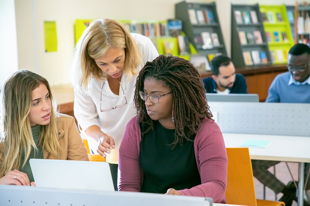 Multiracial group of university students and teacher collaborating on a project in a library setting.