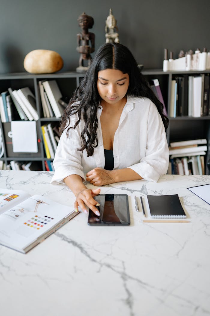 Businesswoman works on a tablet at a stylish office desk with books and notes around.