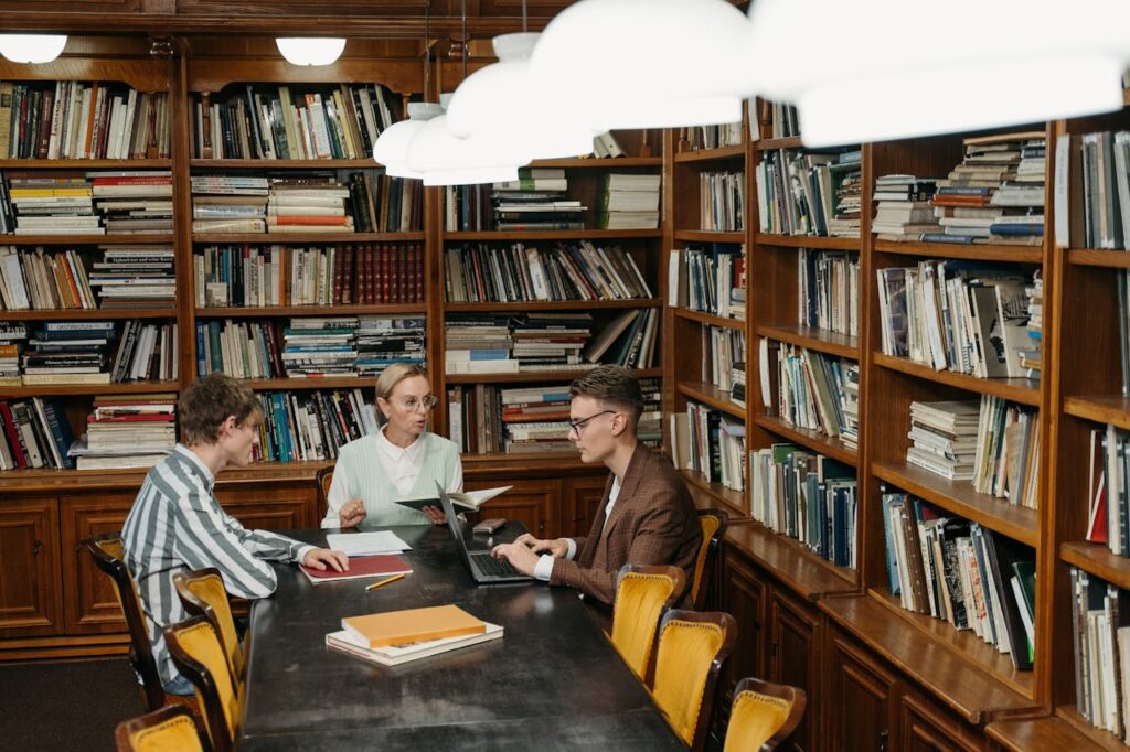 Three professionals having a meeting with laptops and documents in a well-stocked library.