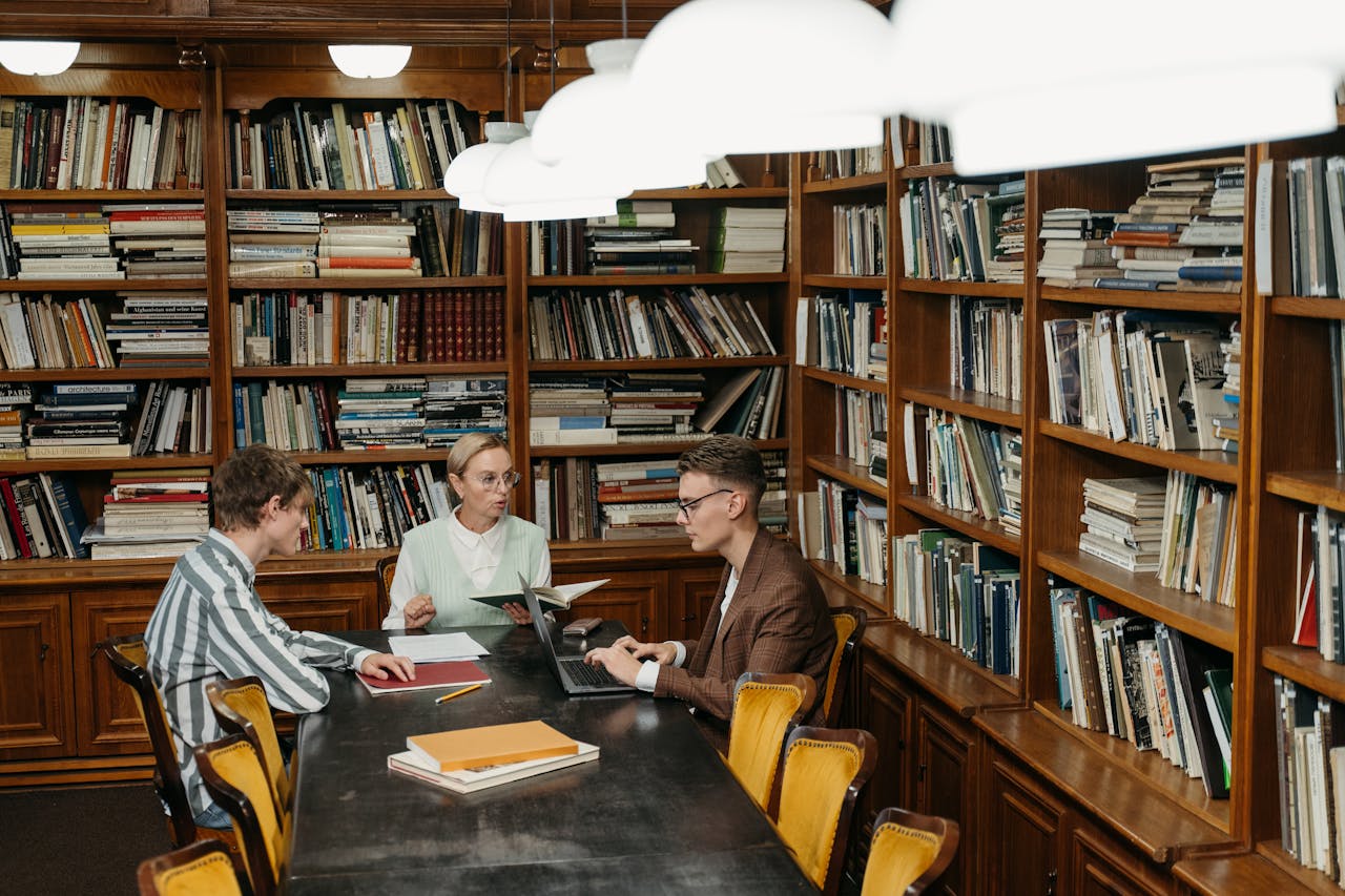 Three professionals having a meeting with laptops and documents in a well-stocked library.